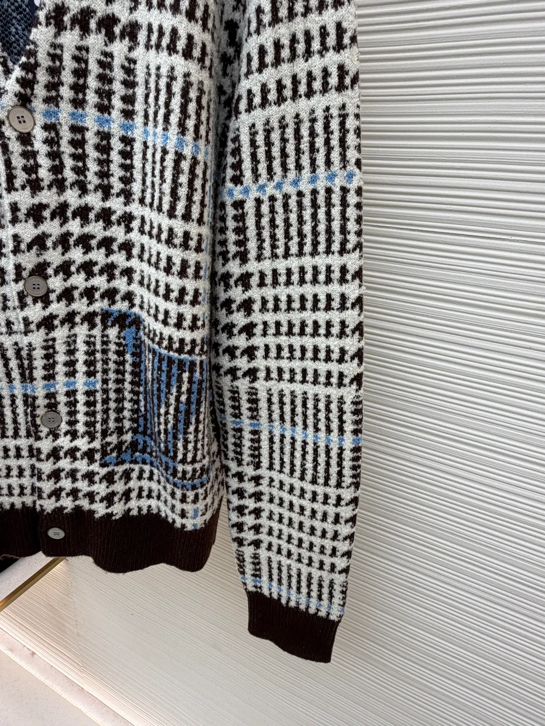 LOUIS VUITTON letter intarsia houndstooth knitted jacquard cardigan ●Original version: purchased and developed by 14743 ●Item number: 1681873-C00 ●Fabric: wool blended fabric ●Technology: jacquard knitting ●Color: black, white and blue ●Version: fitted version ●Weight: about 695 grams ●Size: S-M-L-XL ●Description: The main pattern of this cardigan is woven with full-width jacquard technology, using 69% sheep wool blended with 31% nylon yarn to interweave the houndstooth pattern with light blue line texture. At the same time, the brand logo elements are integrated into the body through intarsia technology, and the edges of the pattern are connected delicately and seamlessly. The collar, cuffs and hem are made of 100% sheep wool ribbed fabric, and are edged with double-needle seaming technology, which has both elasticity and shaping effect. The front placket is equipped with natural-textured buttons, and the side seam pockets use invisible stitching technology to blend naturally with the jacquard texture of the body. The overall shape is shaped through three-dimensional tailoring, and the shoulders are stitched with seamless stitching to ensure fit and comfort. The entire piece is finished with handcrafted details in an Italian workshop, showing the craftsmanship precision of high-quality knitted items. The overall wiring is straight and delicate, the fabric is comfortable and soft, and the color is consistent without color difference. It can be matched with the same style to create a fashionable look and control various occasions. Customized accessories, complete with three standards, same style for men and women!